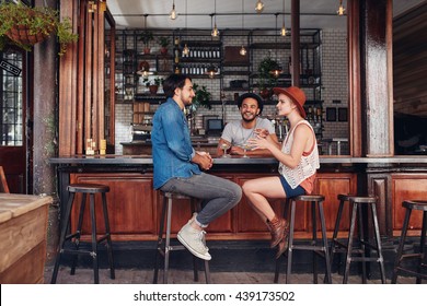 Portrait Of Happy Group Of Young People Meeting In A Coffee Shop And Talking. Three Young Friends Sitting At A Cafe Table.