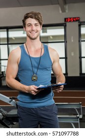 Portrait Of Happy Gym Trainer Standing In Gym With Clipboard