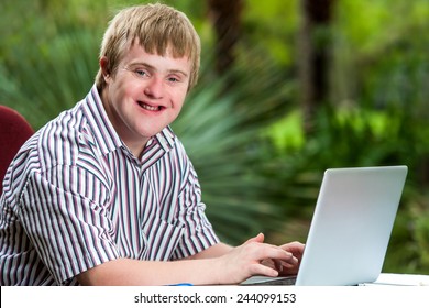 Portrait of happy handicapped young man typing on laptop in garden.