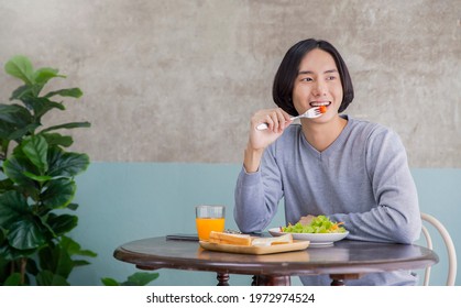 Portrait Of Happy Handsome Asian Man Eating Breakfast In A Cafe Hotel. Young Nerdy Man With Healthy Clean Food Salad And Juice On The Dining Table. Modern Healthy Food Lifestyle Holiday Concept