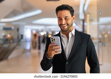 Portrait of happy handsome Hispanic businessman at shopping mall using phone - Powered by Shutterstock