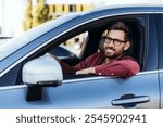 Portrait of happy, handsome Latin man, driver wearing eyeglasses sitting in car, indoors looking at camera. Car, transportation concept