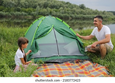 Portrait of happy handsome man wearing casual clothing posing near green tent with his cute daughter, family having camping together, enjoying beautiful nature. - Powered by Shutterstock