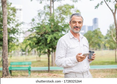 Portrait Of Happy Handsome Older Man Using Smartphone For Business Or Social Media, Attractive Mature Business Men In Casual Lifestyle Checking His Phone While Walking At Park, Banner With Copy Space 