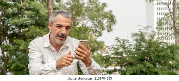 Portrait Of Happy Handsome Older Man Using Smartphone For Business Or Social Media, Attractive Mature Business Men In Casual Lifestyle Checking His Phone While Walking At Park, Banner With Copy Space 