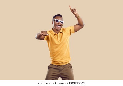Portrait of happy handsome young African American man in casual clothes dancing in fashion studio. Cheerful attractive Tanzanian guy wearing yellow Tshirt and cool sun glasses dancing and having fun