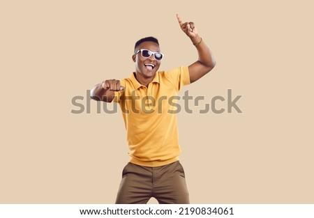 Portrait of happy handsome young African American man in casual clothes dancing in fashion studio. Cheerful attractive Tanzanian guy wearing yellow Tshirt and cool sun glasses dancing and having fun