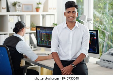 Portrait Of Happy Handsome Young Indian Stock Broker Leaning On Office Table And Smiling At Camera