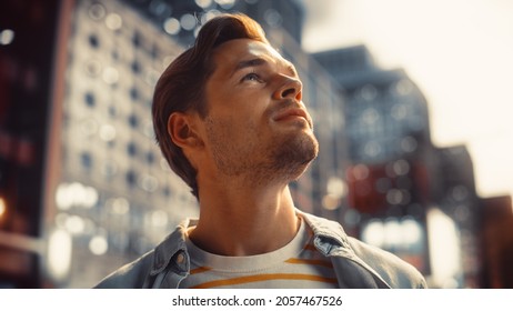 Portrait Of A Happy Handsome Young Man In Casual Clothes Standing On The Street At Sunset. Stylish Male Model In Big City Living The Urban Lifestyle. Background With Office Buildings And Billboards.