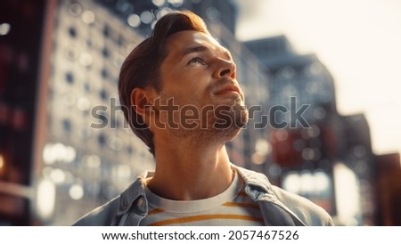Portrait of a Happy Handsome Young Man in Casual Clothes Standing on the Street at Sunset. Stylish Male Model in Big City Living the Urban Lifestyle. Background with Office Buildings and Billboards.