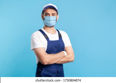 Portrait of happy handyman in overalls mask, and cap standing with crossed hands, profession of service industry, courier delivery. Expert house repairman in workwear smiling. indoor shot isolated