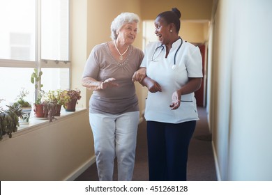 Portrait of happy healthcare worker walking and talking with senior woman. Elder woman gets help from nurse for a walk through nursing home. - Shutterstock ID 451268128