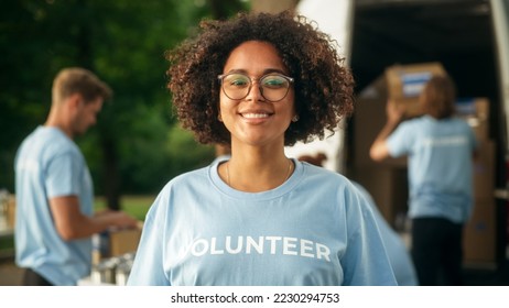 Portrait of a Happy Helpful Black Female Volunteer. Young Adult Multiethnic Latina with Afro Hair, Wearing Glasses, Smiling, Posing for Camera. Humanitarian Aid and Volunteering Concept. - Shutterstock ID 2230294753