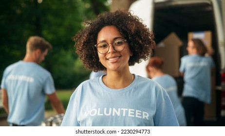 Portrait of a Happy Helpful Black Female Volunteer. Young Adult Multiethnic Latina with Afro Hair, Wearing Glasses, Smiling, Posing for Camera. Humanitarian Aid and Volunteering Concept. - Powered by Shutterstock