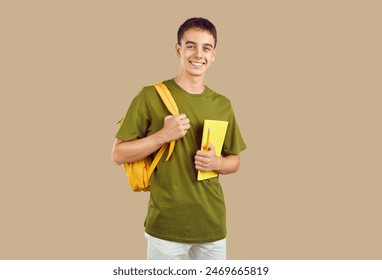 Portrait of happy high school or college student. Young man or teenage boy in casual clothes, with notebook and backpack standing isolated on beige color background, looking at camera and smiling - Powered by Shutterstock