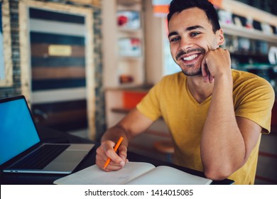 Portrait Of Happy Hipster Guy Looking At Camera And Smiling While Sitting At Desktop With Laptop Computer For E Learning And Textbook For Knowledge Education, Cheerful Male Student Feeling Good