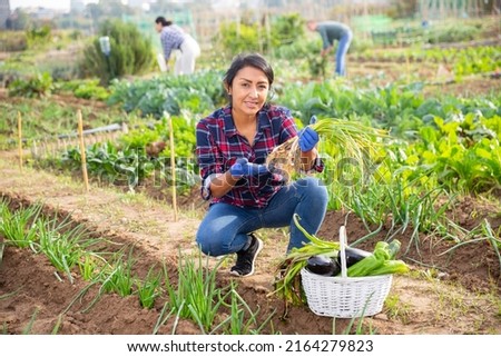 Portrait of happy hispanic woman showing rich crop of vegetables in kitchen garden on sunny fall day
