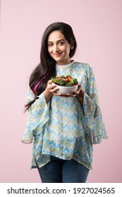 Portrait of a happy Indian asian pretty young woman eating fresh salad from a bowl standing isolated over yellow background