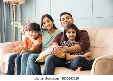 Portrait of happy Indian Asian young family while sitting on sofa, lying on floor or sitting against wall
