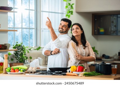 Portrait of Happy Indian asian young couple standing in kitchen with hands folded of presenting something - Powered by Shutterstock