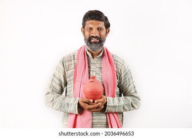 Portrait Of An Happy Indian Bearded Farmer Man In Rural India Concept. Funky Expressions White Background. Saving Money In A Piggy Bank. Cheerful Farmer Happy To Save For The Future.