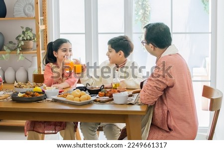 Portrait of happy Indian family, father, son, daughter wearing traditional clothes, sitting at table together for breakfast, lunch or dinner, eating and fun talking with warm. Lifestyle Concept