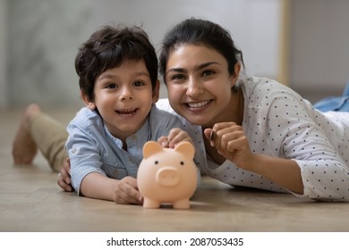 Portrait Of Happy Indian Family Lying On Floor With Small Piggybank. Caring Young Mum Teaching Little Child Son Saving Money For Future Or Planning Purchases, Financial Education Concept.