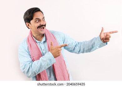 Portrait Of An Happy Indian Farmer In Rural India Concept. Standing In White Background, The Cheerful Farmer Is Pointing Finger Towards The Other Hand. Excited Farmer Is Very Joyous And Exuberant