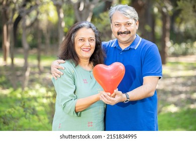 Portrait Of Happy Indian  Healthy Old Couple Holding Red Heart Balloon At Park Outdoor Looking At Camera, Elderly  People Healthcare, Health Insurance