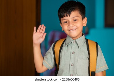 Portrait of a happy Indian little boy in school uniform with backpack waving a hand to the camera with a smile.  - Powered by Shutterstock