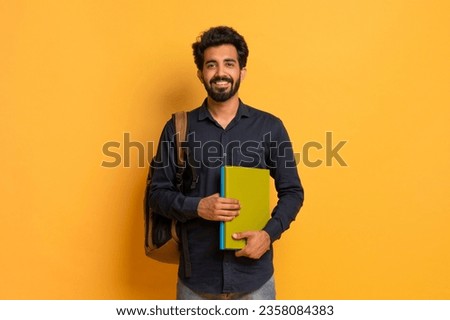 Portrait of happy indian male student with backpack and books posing over yellow studio background, handsome eastern guy holding workbooks and smiling at camera, enjoying modern education, copy space