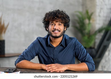 Portrait Of Happy Indian Man Sitting At The Office Desk And Looking At The Camera, Involved In Video Meeting. Webcam View Of Smart Eastern Male In Blue Shirt