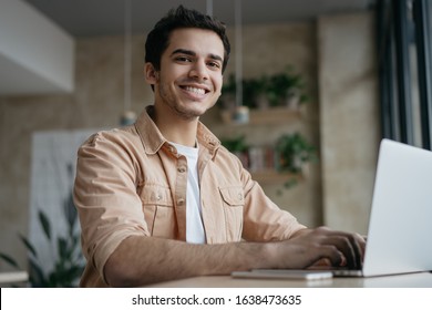 Portrait Of Happy Indian Student Studying, Learning Language. Mixed Race Business Man Using Laptop Computer, Typing On Keyboard, Looking At Camera And Smiling. Copywriter Working From Home