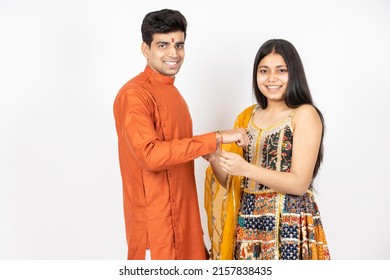 Portrait of happy indian teenage girl tying rakhi on young brother's hand occasion of rakshabandha or bhi dooj isolated on white studio background. both wearing traditional festive cloths.