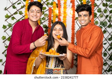 Portrait of happy indian young kids or bothers and sister wearing traditional cloths having fun eating laddu or laddoo sweets celebrating festival  diwali or rakshabandhan, flower decoration. - Shutterstock ID 2158241777