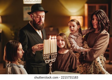 Portrait Of Happy Jewish Family Lighting Menorah Candle During Hanukkah Celebration In Cozy Home