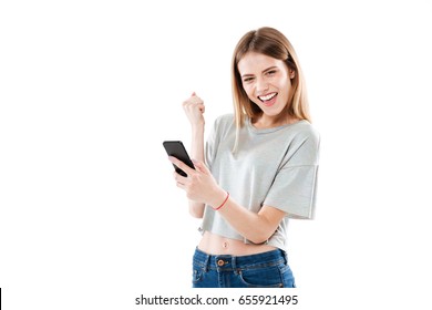 Portrait Of A Happy Joyful Girl Holding Mobile Phone And Celebrating A Win Isolated Over White Background