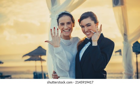 Portrait Of A Happy Just Married Beautiful Lesbian Couple Kissing, Showing Off Their Gold Wedding Rings. Two Attractive Queer Women Smile And Pose For Camera. LGBTQ Relationship And Family Goals.