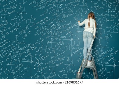 Portrait Of Happy Kid Girl Resolving Complex Math Problem On Blue Chalkboard. Kids Math Education Concept.