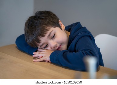 Portrait happy kid lying head down on his arm lookig out with smiling face, Day dream child laying head on table with little smile, Asianyoung  boy sitting alone, Positive children