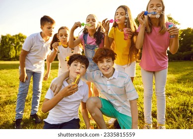 Portrait of happy kids friends standing on green grass in park blowing bubbles together. Group of cheerful children having fun in camp or weekend activity together. Childhood and enjoyment in summer. - Powered by Shutterstock