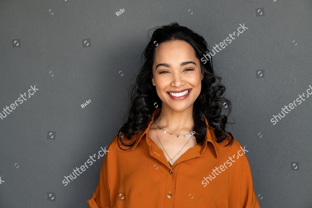 Portrait of happy latin young woman isolated on grey wall with copy space. Carefree hispanic woman smiling and looking at camera standing on gray background. Beautiful multiethnic girl laughing.