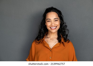 Portrait of happy latin young woman isolated on grey wall with copy space. Carefree hispanic woman smiling and looking at camera standing on gray background. Beautiful multiethnic girl laughing.