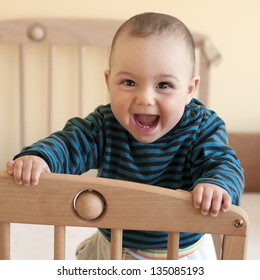 Portrait Of  A Happy Laughing Baby Standing In A Cot.