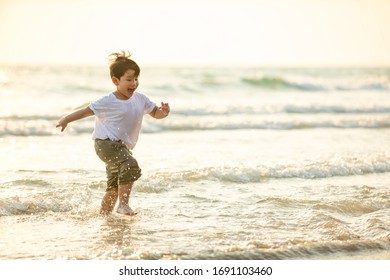 Portrait Happy Little Asian Boy Running And Playing With Smiling And Laughing On Tropical Beach At Sunset. Portrait Of Adorable Young Child Kids Having Fun In Summer Holiday Vacation Travel.