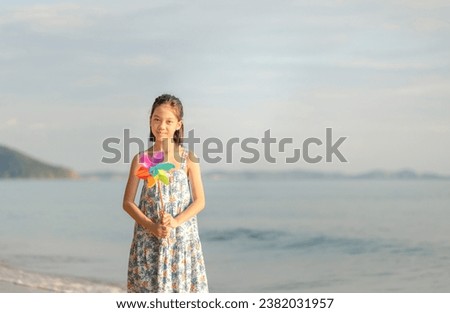 Portrait of Happy little Asian child girl playing on the beach holds windmill in hand, Kid playing outdoors with pinwheels