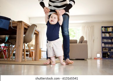 Portrait Of Happy Little Baby Boy Learning To Walk With Mother Help At Home