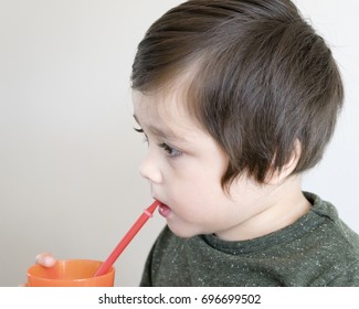 Portrait Of Happy Little Boy Smiling And Drinking Orange Juice With Straw And Holding Orange Plastic Glass, Concept For Healthy Lifestyles Or Healthy Kid