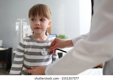 Portrait Of Happy Little Child Standing In Office Of Modern Hospital And Looking Away With Interest. Professional Female Therapist Checking Patients Condition. Health Checkup Concept