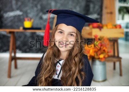 Portrait of happy little girl in graduate headdress. Happy Schoolgirl in master's hat. Smiling Little girl in a school uniform in classroom at school. Back to school. A joyful beautiful graduate. 
